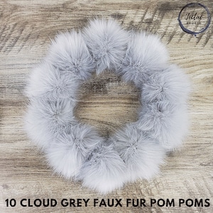 May include: A circular arrangement of ten cloud grey faux fur pom poms. The pom poms are fluffy and soft, with a light grey color. The text "10 CLOUD GREY FAUX FUR POM POMS" is at the bottom of the image.
