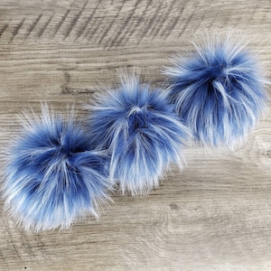 May include: Three blue and white faux fur pom poms. The pom poms are fluffy and soft, and they would be perfect for adding a touch of whimsy to a hat or scarf.
