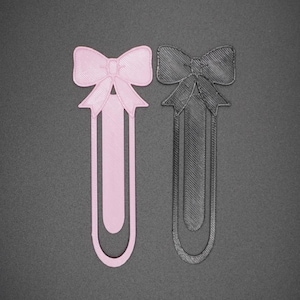 May include: Two 3D printed bookmark designs, one pink and one black, shaped like bows with a long, thin, rectangular base.