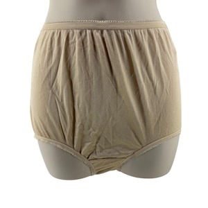 Puede incluir: Ropa interior de color beige con cintura alta y textura suave y lisa. La cintura elástica y las aberturas de las piernas están ribeteadas con un delicado borde festoneado. La ropa interior se muestra en un maniquí.