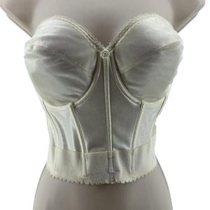 May include: Ivory-colored bustier with a sweetheart neckline and scalloped trim. The vintage lingerie piece features structured cups, vertical boning, and a decorative floral accent at the center. A classic, elegant design.