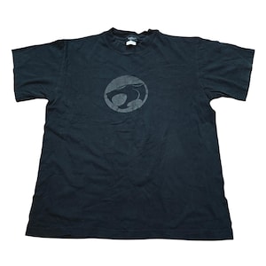 Puede incluir: Camiseta negra con un gráfico gris circular de una cabeza de gato estilizada. La camiseta tiene mangas cortas y cuello redondo. El gráfico está centrado en el pecho. La camiseta está hecha de un material suave, probablemente algodón.