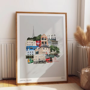 May include: A framed print of a collage of buildings and transport in Crystal Palace, London. The collage features a red double-decker bus, a green train, and various buildings in different colours.