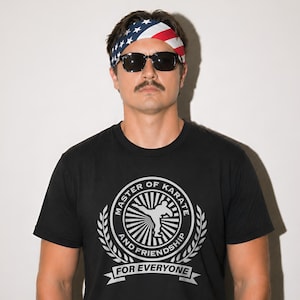May include: Black t-shirt with a white graphic that reads "MASTER OF KARATE AND FRIENDSHIP FOR EVERYONE." The person is wearing a headband with the American flag design and black sunglasses.
