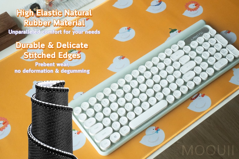 May include: A white keyboard with round keys and a light blue frame sits on a yellow mousepad with a pattern of white cartoon ducks. The mousepad has the text "MOOUII" in the bottom right corner. The text "High Elastic Natural Rubber Material" and "Durable & Delicate Stitched Edges" is printed on the mousepad.