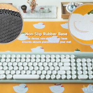 May include: A light blue keyboard with round white keys and a non-slip rubber base. The keyboard is on a yellow desk mat with a white duck design. The text "Non-Slip Rubber Base" is written in black on the mat. The text "The dense, non-skid rubber base ensures secure placement of your mat" is written in black below the title.