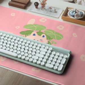 May include: A pink desk mat with a white cat illustration and a light green keyboard. The mat has a floral pattern with white flowers.