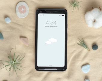 May include: A black smartphone with a white background and two white clouds on the screen. The time is 4:34 and the date is Monday, September 30. The phone is lying on a beige surface with small decorative objects around it.