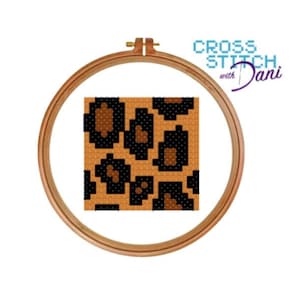 May include: A cross stitch pattern of a leopard print design in brown and black colours. The pattern is displayed in a wooden embroidery hoop.