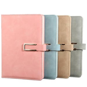 May include: Four pastel-colored journals with gold-tone clasps. The journals are in shades of pink, blue, tan, and gray. Each journal has a rectangular shape with a stitched border and a clasp closure.