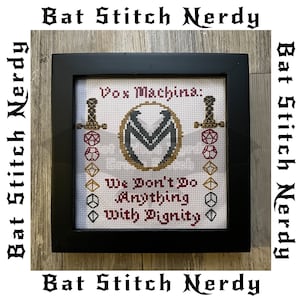 Pode incluir: Um design de ponto cruz emoldurado com o logotipo do Vox Machina e a citação "We Don't Do Anything With Dignity". O logotipo é um "M" estilizado em preto e cinza com um círculo dourado ao redor. A citação está em preto e branco com acentos vermelhos. O fundo é branco com uma borda vermelha e dourada.