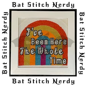 May include: A framed cross-stitch design with a rainbow background and the text "I've Been Here The Whole Time".
