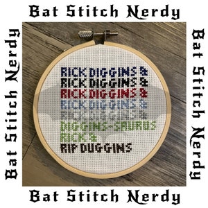 May include: A white embroidery hoop with a cross-stitch design that reads "RICK DIGGINS & DIGGINS-SAURUS RIP DUGGINS". The design is in red, blue, and green thread.