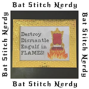 Może przedstawiać: Sztuka haftu krzyżykowego w złotej ramie z napisem "Destroy, Dismantle, Engulf in FLAMES!" i tronem w płomieniach. Słowa "Bat Stitch Nerdy" są wydrukowane wokół ramy.