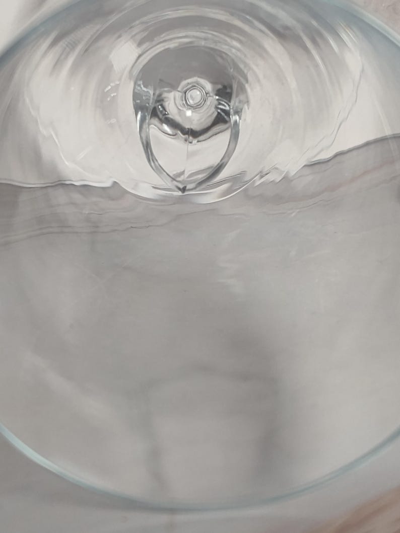 May include: A clear glass object with a rounded base and a heart-shaped design in the center. The glass has a smooth, reflective surface, and the image is taken from a top-down perspective, creating a sense of depth.