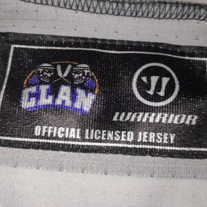 May include: Black and white label with the text "CLAN" in a purple and white logo with two hockey players. The label also has the text "WARRIOR" and "OFFICIAL LICENSED JERSEY".