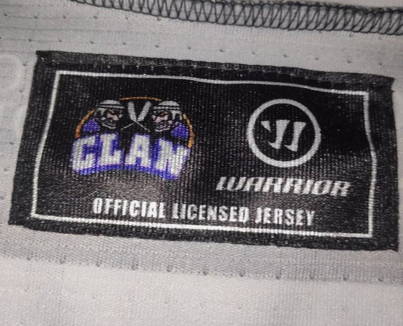 May include: Black and white label with the text "CLAN" in a purple and white logo with two hockey players. The label also has the text "WARRIOR" and "OFFICIAL LICENSED JERSEY".