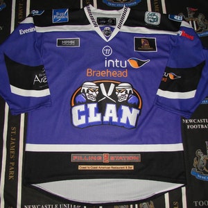 May include: Purple hockey jersey with black and white trim. The front of the jersey features a large logo with two hockey players wearing helmets and the word "CLAN" in blue. The jersey also has the words "intu Braehead" and "Filling Station" on the front.