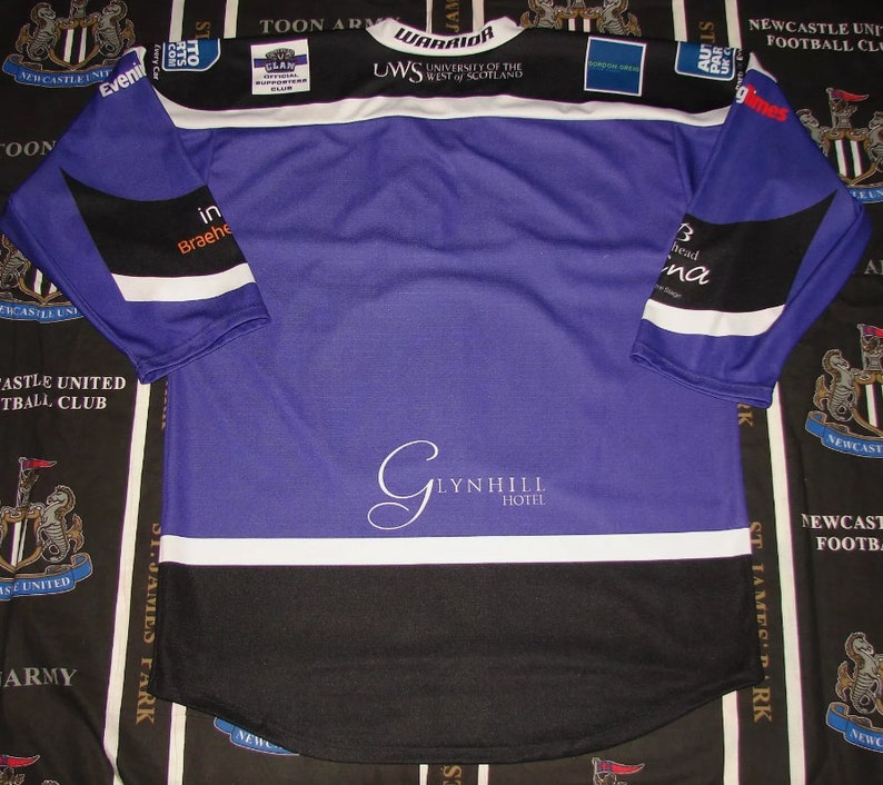 May include: A purple and black long-sleeved jersey with white accents. The jersey has the text "WARRIOR" and "UWS UNIVERSITY OF THE WEST OF SCOTLAND" on the front. The jersey also has the text "GLYNHILL HOTEL" on the front.