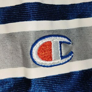 Puede incluir: Una tela a rayas blancas, grises y azules con un logotipo "C" bordado en azul, blanco y rojo.