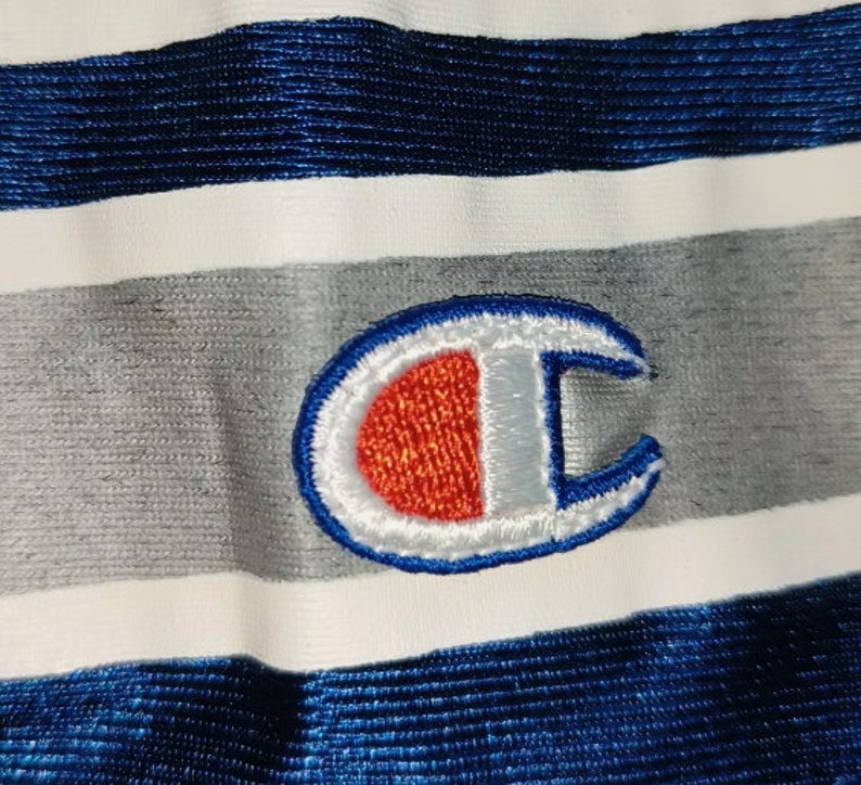 Puede incluir: Una tela a rayas blancas, grises y azules con un logotipo "C" bordado en azul, blanco y rojo.
