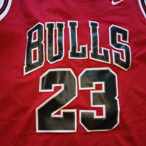 Puede incluir: Camiseta de baloncesto roja con letras negras y blancas que dicen "BULLS" y el n&uacute;mero "23" en la parte delantera.
