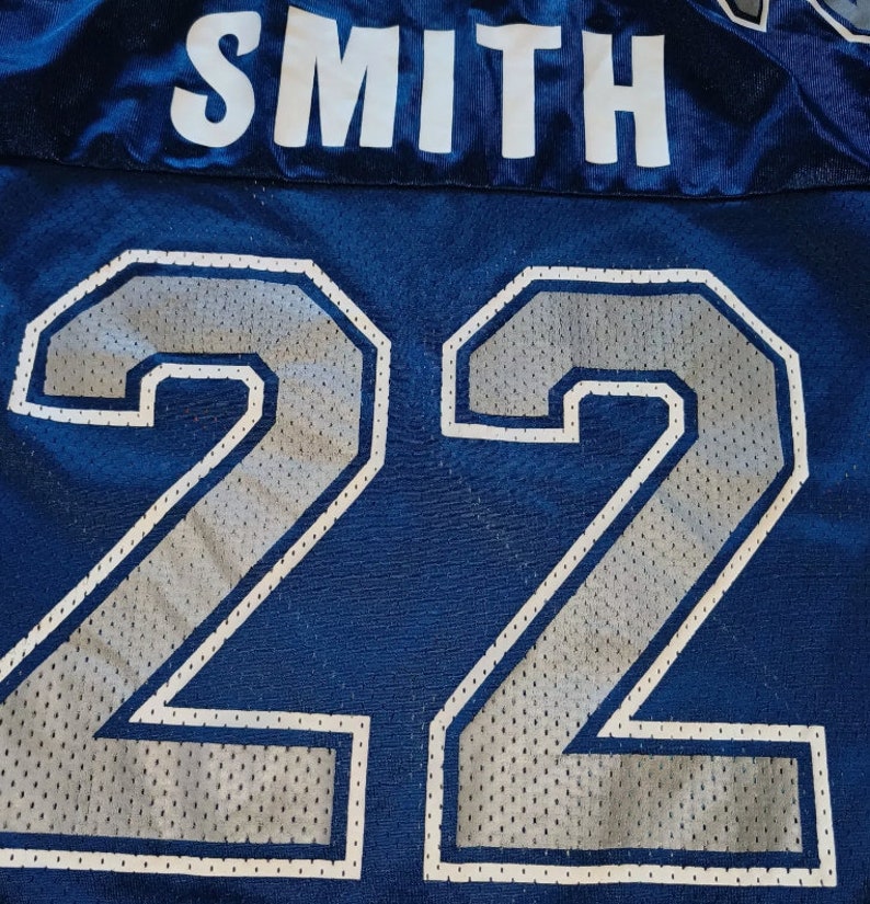 Puede incluir: Una camiseta azul con el nombre "SMITH" y el n&uacute;mero "22" en blanco con un patr&oacute;n de malla plateada.