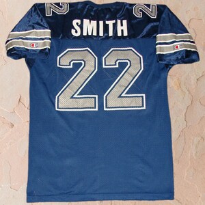 Puede incluir: Una camiseta de f&uacute;tbol azul marino con el n&uacute;mero 22 y el nombre "SMITH" en la espalda. La camiseta tiene ribetes blancos y plateados y un logotipo de Champion en la manga.