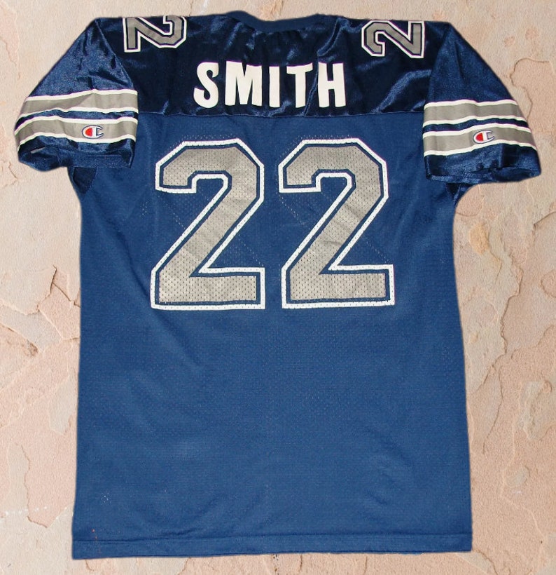 Puede incluir: Una camiseta de f&uacute;tbol azul marino con el n&uacute;mero 22 y el nombre "SMITH" en la espalda. La camiseta tiene ribetes blancos y plateados y un logotipo de Champion en la manga.
