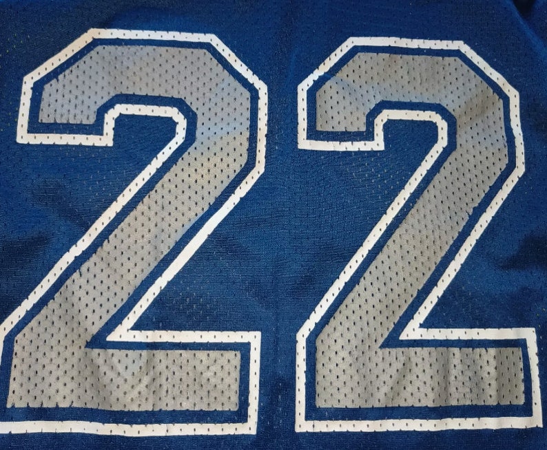 Puede incluir: Primer plano de una camiseta azul con el n&uacute;mero 22 en blanco bordeado de plata.