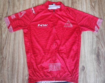 May include: Red cycling jersey with a white zipper and white logo that says "NW Cycling Since 93". The jersey has a white triangle with the text "Enjoy Tour Ride" on the right side of the chest.