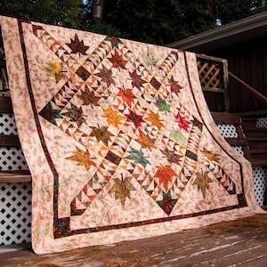 May include: A quilt with a patchwork design featuring a variety of fall colors, including brown, orange, red, and green. The quilt is made up of squares and triangles, and it features a pattern of leaves.
