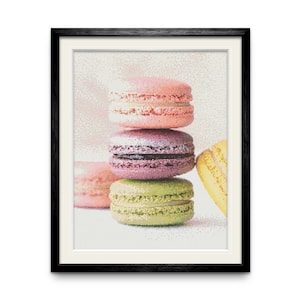 Op de afbeelding: Een stapel van vier kleurrijke macarons. De macarons zijn gerangschikt in een piramidevorm, met de grootste macaron onderaan en de kleinste macaron bovenaan. De macarons zijn roze, paars, groen en geel.