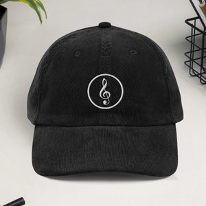 Puede incluir: Gorra de béisbol de pana negra con un logotipo de clave de sol bordado en blanco. La gorra tiene una visera curva y un diseño de seis paneles. Un accesorio elegante para los amantes de la música.