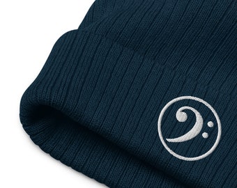 May include: A dark blue knitted beanie with a white embroidered bass clef symbol in a circle.