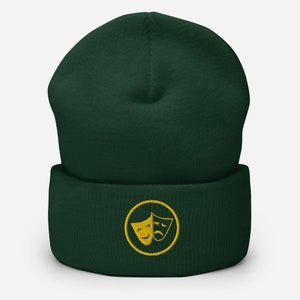 Peut inclure: Un bonnet vert foncé avec un cercle brodé en or contenant deux masques de théâtre, l'un souriant et l'autre fronçant les sourcils.