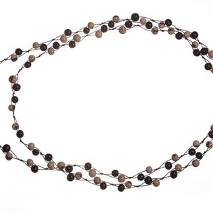 Op de afbeelding: Een ketting met meerdere strengen kleine, ronde kralen in bruine en beige tinten. De kralen zijn geregen op een donker koord, wat een gelaagd effect creëert. De ketting wordt gepresenteerd tegen een witte achtergrond.