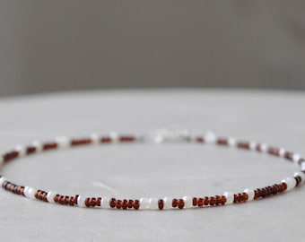 May include: Delicate beaded necklace featuring alternating white and dark red beads. The necklace is strung on a thin, flexible cord and has a silver-colored clasp. This piece of jewelry is suitable for everyday wear.