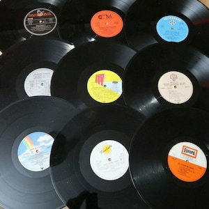 Op de afbeelding: Een verzameling van tien zwarte vinylplaten met verschillende labels en titels. De labels hebben verschillende kleuren, ontwerpen en tekst.