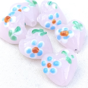May include: Six pink glass heart-shaped beads with white, blue, and orange floral designs.