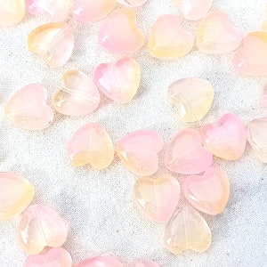 May include: A collection of heart-shaped beads in shades of pink and yellow. The beads are translucent and have a glossy finish.