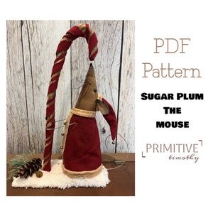 Puede incluir: Patrón PDF para una muñeca de ratón primitiva hecha a mano llamada "Sugar Plum The Mouse" de Primitive Timothy. El ratón lleva un traje de Papá Noel rojo y blanco y sostiene un bastón de caramelo.