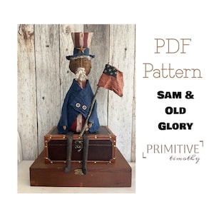 May include: A handmade rag doll dressed as Uncle Sam, holding a small American flag. The doll is sitting on a wooden chest with a brown leather top. The doll is wearing a blue jacket, red trousers, and a white hat with red and blue stripes. The doll has a white beard and a brown face. The image includes the text "PDF Pattern Sam & Old Glory Primitive Timothy".