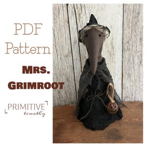 May include: A handmade Mrs. Grimroot doll with a long, beak-like nose, wearing a black cloak and hat. The doll holds a small pumpkin. The image includes the text "PDF Pattern" and "Primitive Timothy".