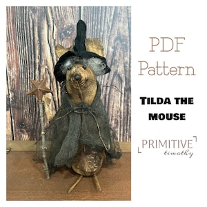 Könnte beinhalten: Ein PDF-Muster für eine Tilda the Mouse Primitive-Puppe. Die Puppe trägt einen schwarzen Hexenhut und einen schwarzen Umhang. Die Puppe hält einen Stock mit einem Stern oben drauf. Das Muster ist von Primitive Timothy.