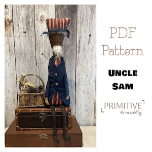 May include: A PDF pattern for a primitive doll, Uncle Sam, wearing a red, white and blue hat and a blue jacket. The doll is sitting on a wooden box with a basket of twigs and pine cones beside it. The text "PDF Pattern Uncle Sam Primitive Timothy" is visible in the image.