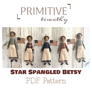 Può includere: Cinque bambole fatte a mano con grembiuli e vestiti di stoffa sono appese in fila, con piccole bandiere americane tra loro. Le bambole hanno i capelli castani e sono vestite con vari colori. È visibile anche il testo "PRIMITIVE timothy" e "STAR SPANGLED BETSY PDF Pattern".