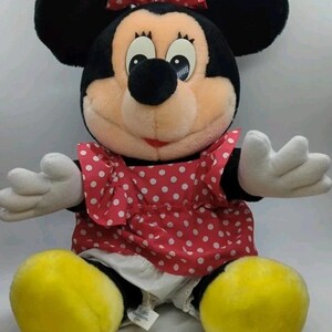 May include: A plush Minnie Mouse doll with black ears, a red polka-dot dress, and a matching bow. The doll has white gloves and yellow shoes. The doll is a classic Disney character.