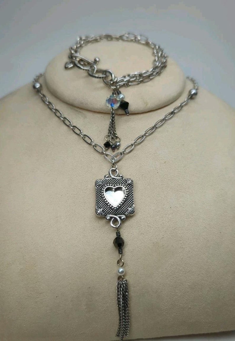 Peut inclure: Ensemble collier et bracelet argent&eacute;. Le collier pr&eacute;sente un pendentif carr&eacute; avec une d&eacute;coupe en forme de c&oelig;ur, une perle noire pendante et une pampille en cha&icirc;ne. Le bracelet a un fermoir &agrave; bascule et un design en cha&icirc;ne.