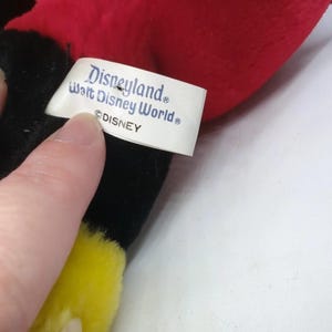May include: A plush toy with red, black, and yellow accents. The tag reads "Disneyland Walt Disney World &copy;DISNEY". The toy is soft and appears to be a character from Disney.
